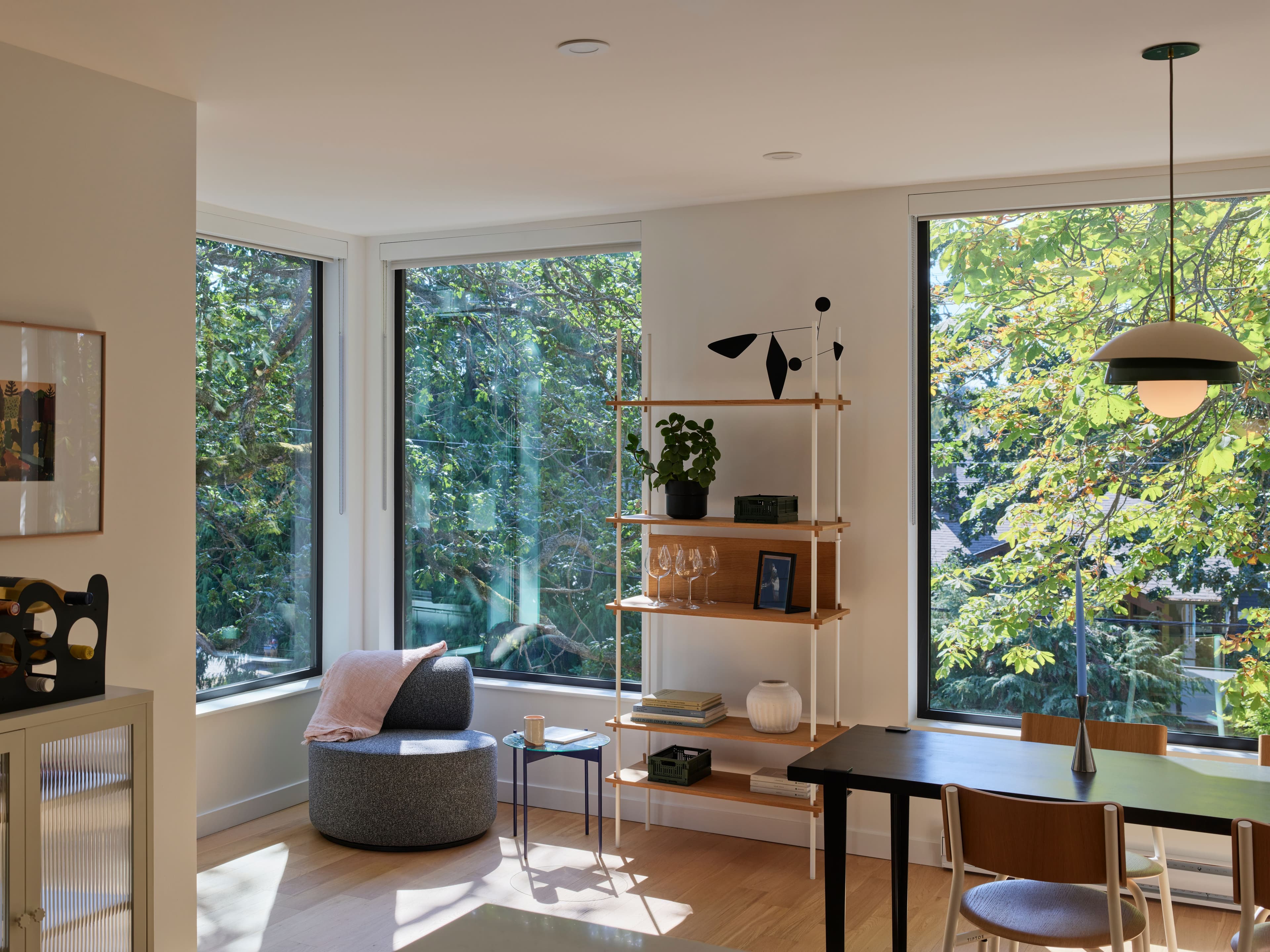Bright corner living and dining space in a Wisteria Row townhome in Victoria BC, with large windows that look out onto leafy treetops.